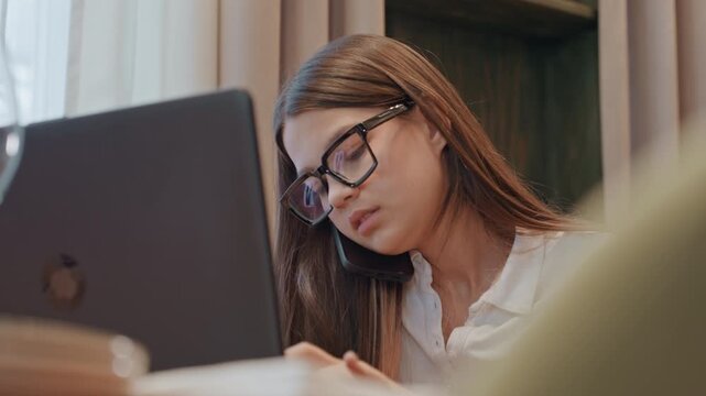 Woman focused on laptop and notes, cozy cafe study setting with glasses, soft window light, coffee cup, notebook, typing and reading, calm concentration and productivity vibe, remote student preparing