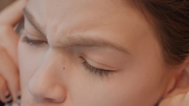 Closeup phone forehead and eyes show fatigue and worry young woman handling difficult conversation with slow breath and hand supporting head, downward gaze, muted color palette, intimate portrait