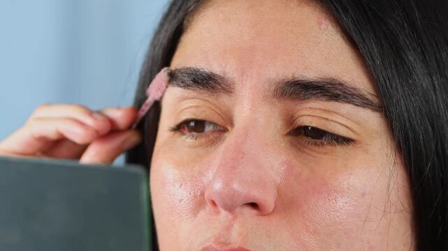 Beautiful young woman using eyebrow mascara gel to shape and define her brows during a personal beauty and self care routine indoors