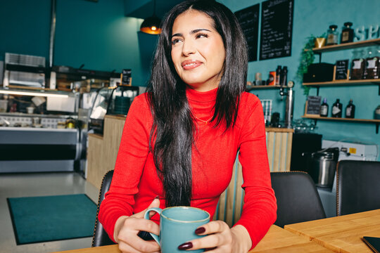 Smiling woman in red turtleneck enjoys coffee at a cozy cafe setting