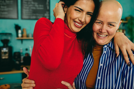Young diverse woman hugging her bald friend and smiling in a cozy cafe showing support and friendship