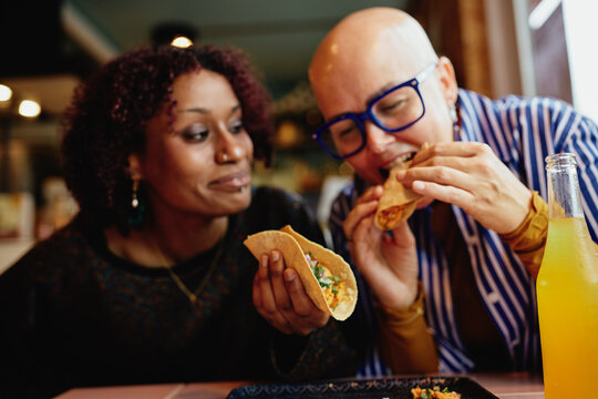 Two diverse friends enjoying tacos and soda at a casual restaurant, sharing a joyful meal together. 