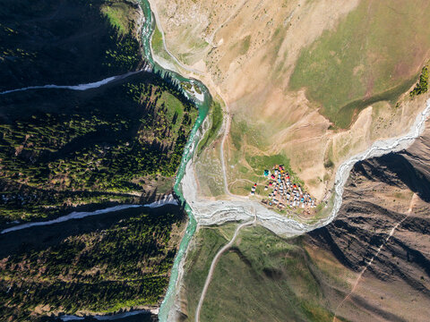 High altitude remote settlement in a rugged valley where teal glacial waters meet rocky tributaries under the shadows of the Karakoram and Himalayan peaks
