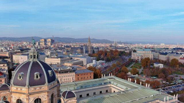 4K aerial view of Vienna with Kunsthistorisches Museum dome, Rathaus city hall gothic spire, Burgtheater, Votivkirche and Volksgarten on the Ringstrasse with Vienna Woods backdrop in autumn.