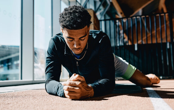 Low angle view of a fit strong black young man in sportswear focused on a leg workout while lying on an exercise mat on the floor of a sunny gym