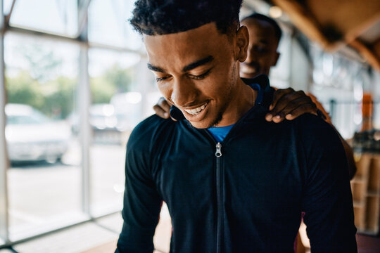 Fit young african american man laughing while getting a pat on the back from his trainer after a workout session together in a gym