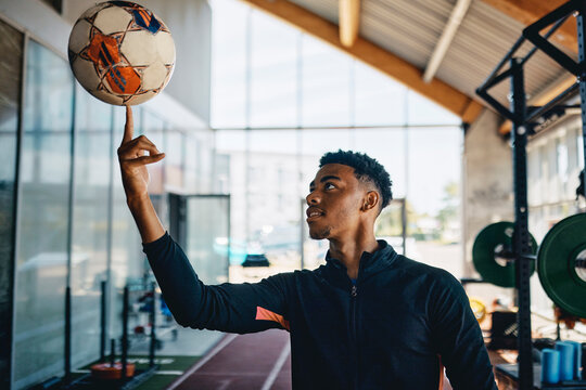 Fit young black sporty man in sportswear smiling while spinning a ball on his fingertip during a break between workouts in a gym