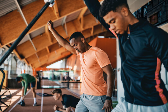 A african american trainer teaching a fit young man how to workout with a barbell during a strength training workout session in a gym