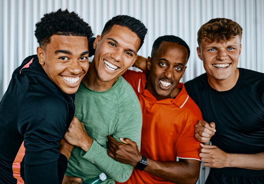 Diverse group of fit young men in sportswear laughing and messing around while standing arm in arm together in a gym after an exercise class together