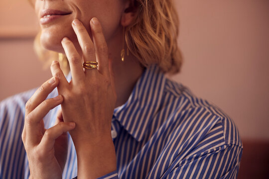 Woman in a striped blue shirt touches her lips. Close-up of a ring on her finger and earrings hanging from her ear.