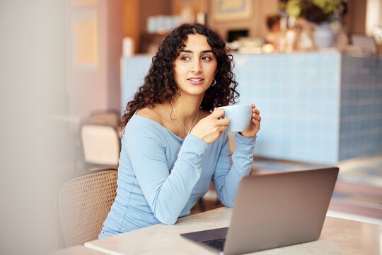 Relaxed cafe moment. Black strong woman drinking coffee beside a laptop, feeling focused and confident