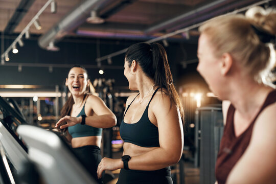 Laughing diverse group of fit young women in sportswear riding on stationary bikes during a cardio workout class together in a health club