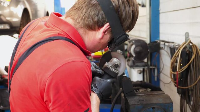 Skilled technician in red shirt and gloves meticulously grinds metal component in garage, showcasing precision and focus in automotive repair process with sparks flying