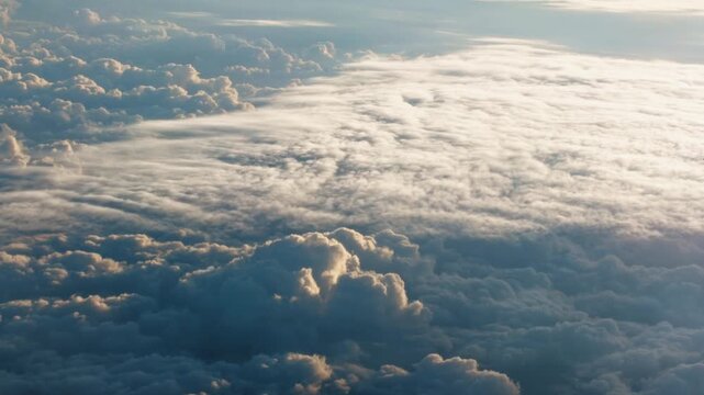 High-altitude aerial view of a vast cloudscape, a thick, rippling stratocumulus cloud deck meeting larger, towering cumulus formations, all illuminated by the soft, warm light of a low-angle sun.