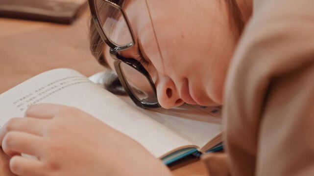 Resting student dozing. Student sleeps quietly amid studying. Silent late evening revision as student rests peacefully. Calm and quiet workspace with student dozing over open book at night