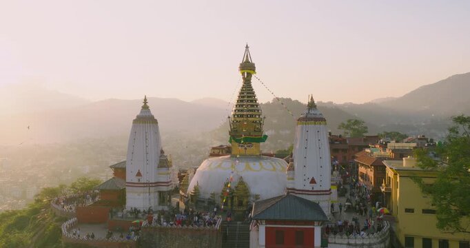 An aerial pull-out view revealing Swayambhunath Monkey Temple and Kathmandu Valley, Nepal, during golden sunset light with a golden sky and urban city.