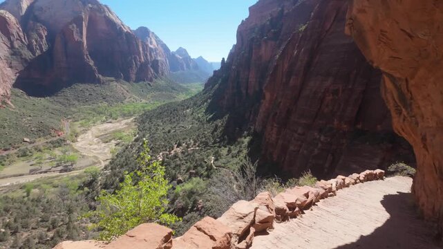 Hiking on a trail on the edge of a mountain looking over the valley of Zion National Park and the Virgin River.