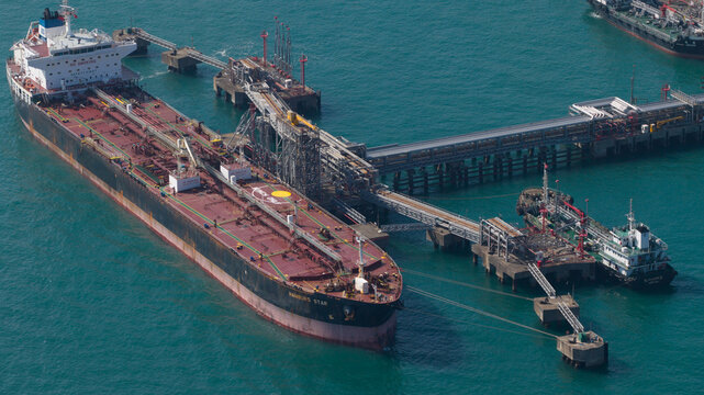 Aerial view of a large oil tanker docked at an industrial offshore terminal with complex piping systems and turquoise water Hong Kong, Hong Kong.