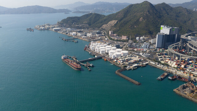 Aerial view of industrial oil storage tanks and a large tanker ship docked at the terminal near green mountains and a highway viaduct Hong Kong, Hong Kong.
