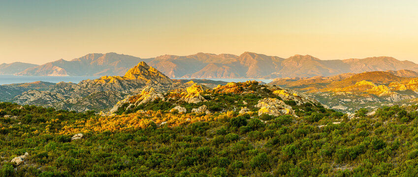 Corsica Agriates desert landscape featuring rocky hills, green maquis, and distant sea under golden light, an ideal tourism destination for exploration with copy space.