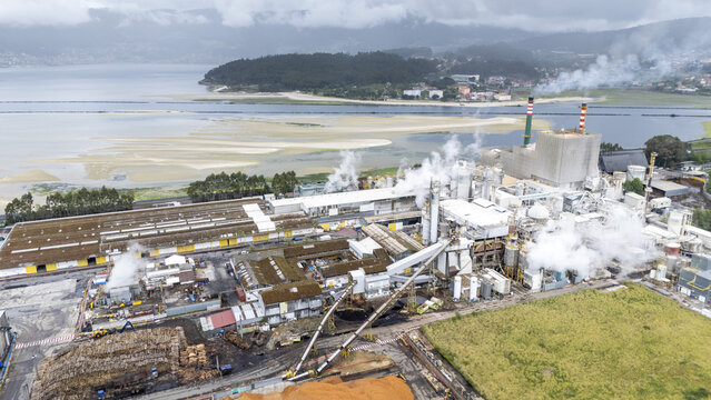 Aerial view of Biofabrica de Ence en Pontevedra with smoking chimneys and industrial structures near the estuary under a cloudy sky Pontevedra, Pontevedra, Spain.