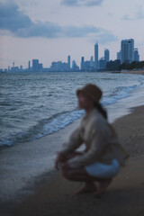 Fototapeta premium Vertical blurred image of a woman sitting by the sea with stormy sky