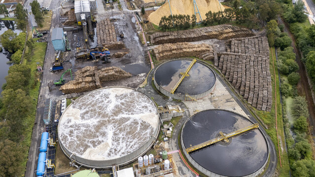 Aerial view of the Biofabrica de Ence industrial plant with large circular treatment tanks, massive stacks of timber, and machinery in Pontevedra, Pontevedra, Spain.