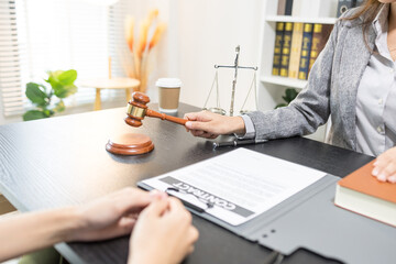 Fototapeta premium Two women sit at a desk, engaged in a serious conversation. One holds a book and a small statue, gesturing thoughtfully. The other listens intently, hands clasped near her chest 