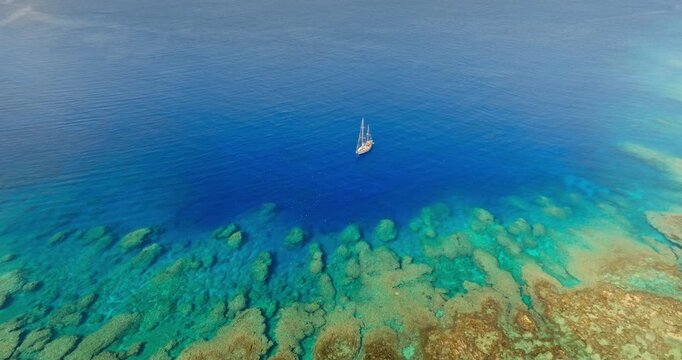 Sailboat navigating vibrant turquoise ocean water, drifting alongside a colorful coral reef, revealing the stunning underwater landscape of the Torres Islands, Vanuatu. Aerial view zoom in panorama