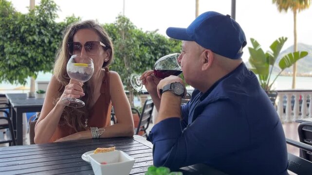 Pareja brindando con sus copas y bebiendo en una terraza del paseo mar&iacute;timo