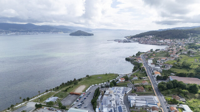 Aerial view of the coastal town of Casalvito featuring the bay with a small island and lush green hills under a cloudy sky in Casalvito, Pontevedra, Spain.
