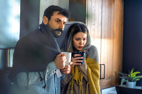 Freezing couple covered with a blanket. Man and a woman wrapped in a warm blanket in a cold room.