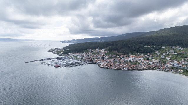 Aerial view of the historic coastal village of Combarro featuring its marina, traditional stone architecture, and green hills under a cloudy sky in Combarro, Pontevedra, Spain.