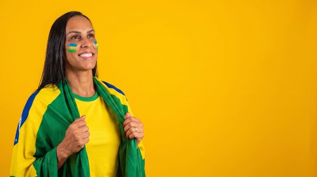 Happy Brazilian female supporter wearing a yellow jersey and flag, with face paint in national colors, celebrating a sports victory or national holiday on a vibrant yellow background