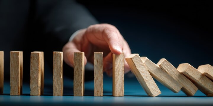 Hand stopping domino effect, symbolizing risk management and crisis prevention.