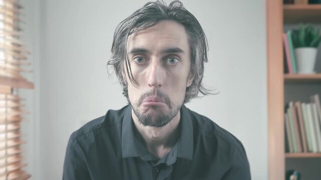Approvingly Close-Up of a Man with Long Hair in a Dark Shirt Engaged in Introspection, Expressing Surprise and Contemplation Against a Neutral Background