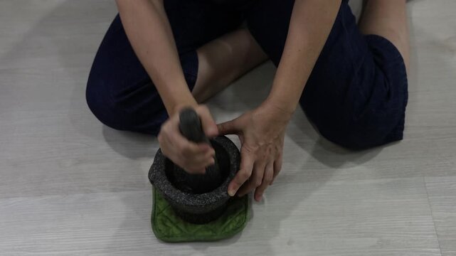 Asian housewife is pounding garlic in traditional stone mortar. (Angsila stone mortar. Use granite pestle to finely grind garlic for cooking.) Pounding spice mixture for Thai food. Thai granite mortar