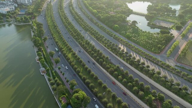 Aerial drone view of tree lined boulevard beside lakes and green urban landscape in western Hanoi during golden morning light.