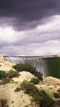 Water flowing over the lake bard dam spillway after a storm in simi valley, california, creating an impressive cascade and waterfall against a cloudy dramatic sky