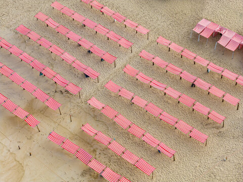 Aerial view of rows of red and white striped beach tents on the sandy shore of Praia de Sao Pedro de Moel in Marinha Grande, Leiria, Portugal.