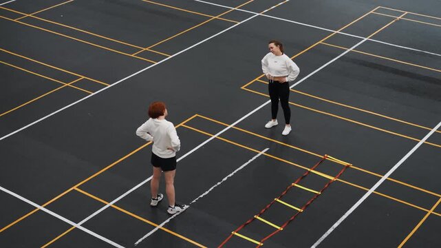Players practicing footwork. Trainees honing footwork techniques under coaching guidance during practice. Two athletes engage in precise footwork sessions on marked court with focused supervision