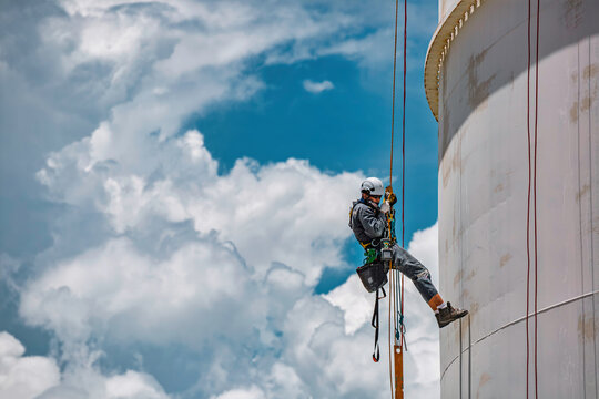 Male worker rope access industrial working at height tank oil wearing harness, helmet safety equipment rope access inspection of thickness