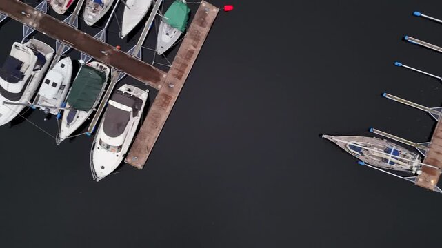 Impressive aerial top down view of a sailboat performing a skillful reverse maneuver to dock perfectly into its berth at a quiet and modern marina surrounded by other luxury yachts
