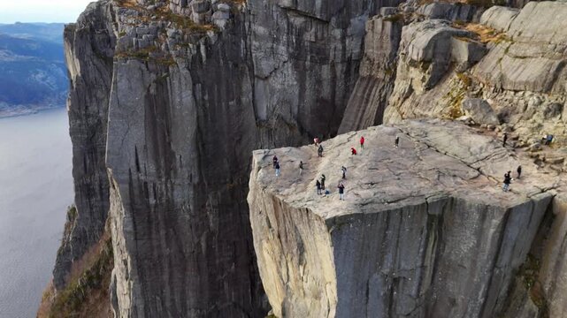 Breathtaking aerial footage orbiting the iconic preikestolen, or pulpit rock, where numerous tourists are admiring the spectacular panoramic view of the lysefjord in rogaland county, norway