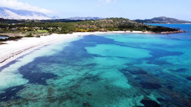 Aerial view along the shore of Lu Impostu beach with turquoise water white sand and Mediterranean coastline in Sardinia on a sunny day
