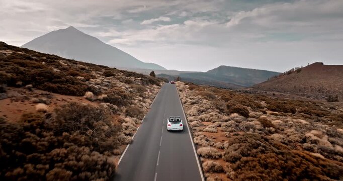 White convertible car driving long winding road through the volcanic landscape of Teide National Park, a couple enjoying their road trip in the Canary Islands. Aerial view drone flight tracking shot
