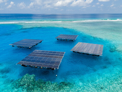 Aerial view of SolarSea floating solar power plant platforms on turquoise lagoon water near a coral reef in Dharavandhoo, Baa Atoll, Maldives.