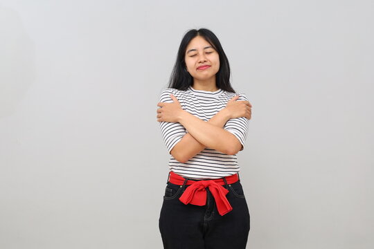 A young Asian woman smiling happily, peacefully, calmly and contentedly, proud of herself, hugging herself, closing her eyes, isolated on a white background.
