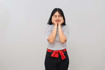 A young Asian woman stands alone against a white background, looking frustrated and covering her ears. © ArvStd