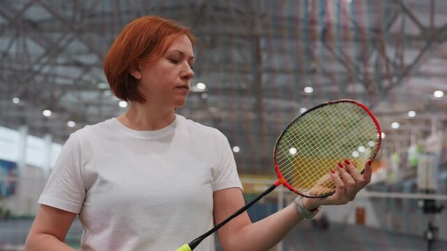 Indoor court training white woman adjusting grip, demonstrating technique to small group, calm reflective expression, fluorescent lights, sports arena background, equipment check and light repairs